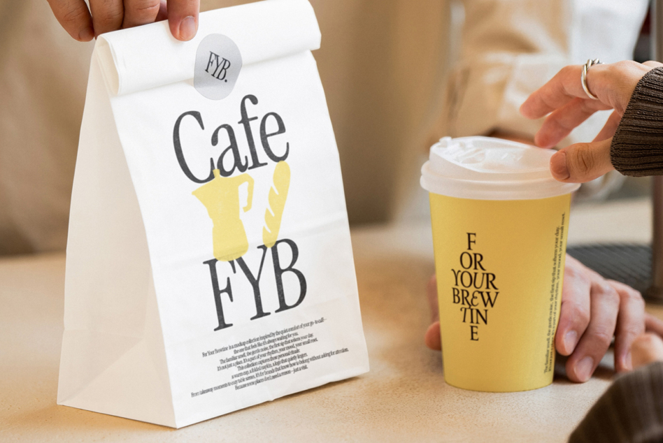 White paper bag with Cafe FYB branding held in hand next to yellow cup with sticker