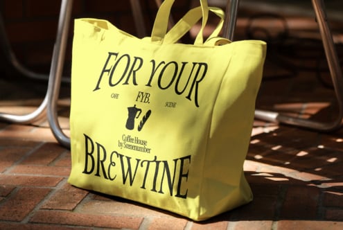 Bright yellow tote bag with For Your Brew Wine text on brick ground