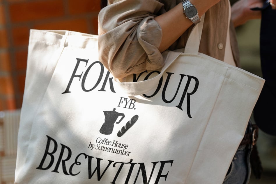 Cream colored tote bag with black coffee logo design held by person