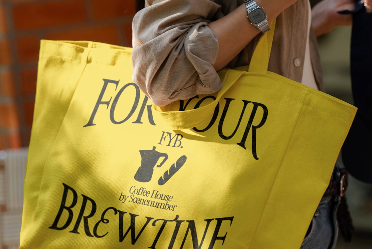 Bright yellow tote bag with coffee shop branding held by person in neutral outfit