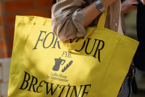 Bright yellow tote bag with coffee shop branding held by person in neutral outfit