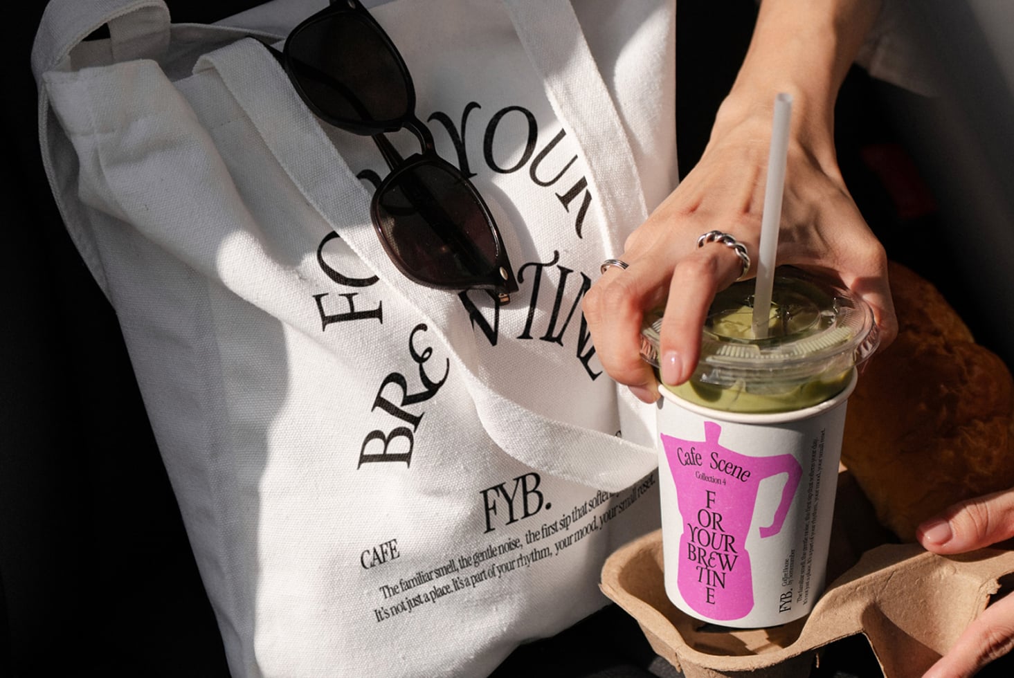 Hands holding white tote bag with sunglasses, holding pink branded coffee cup