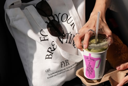 Hands holding white tote bag with sunglasses, holding pink branded coffee cup