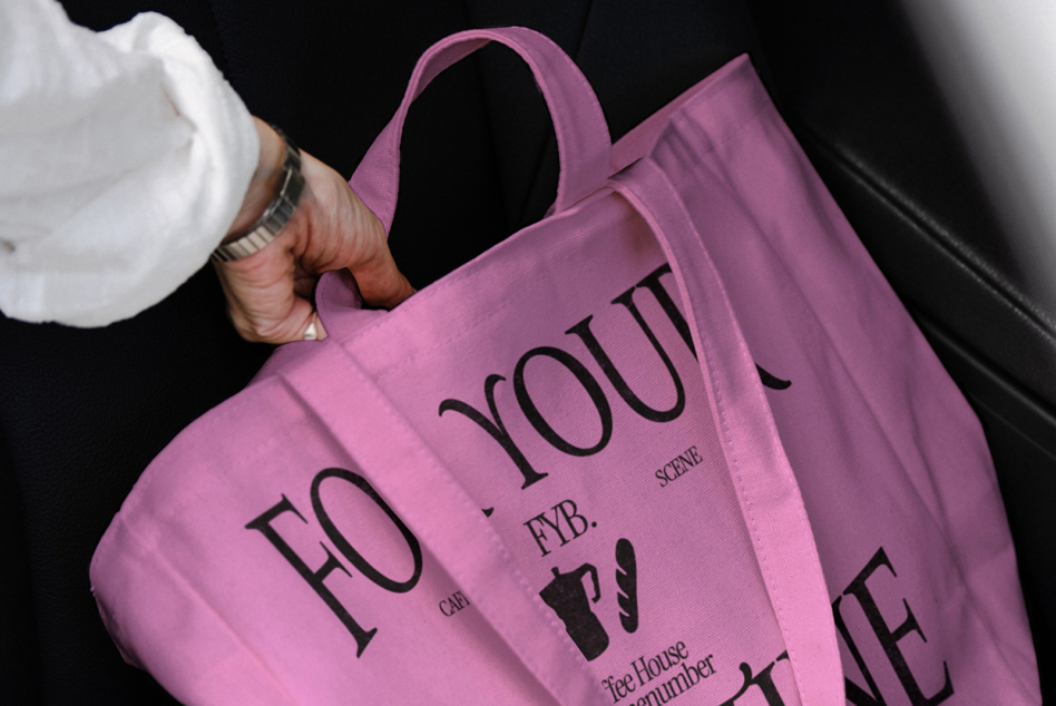 Mauve pink tote bag displaying cafe scene typography held by hands