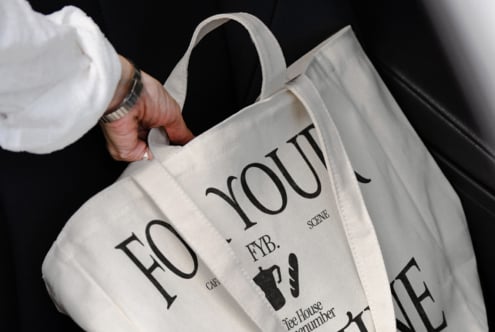 Hand holding white tote bag with black text reading For You Cafe FYB Scene