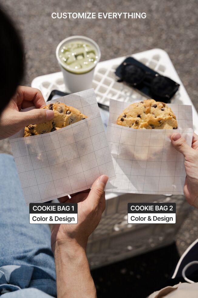 Two hands holding chocolate chip cookie bags with grid pattern paper over table setting