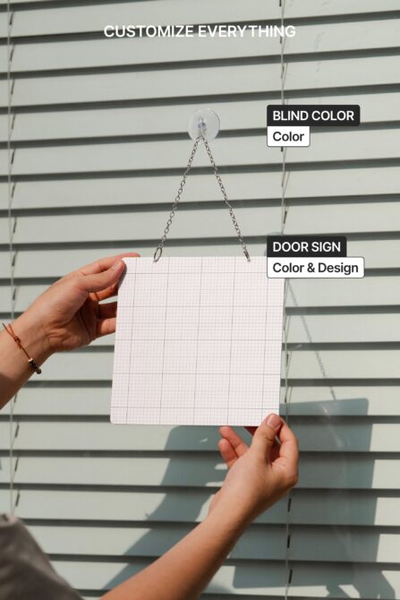 Hand holding blank pink grid paper door sign hanging on chain against striped background