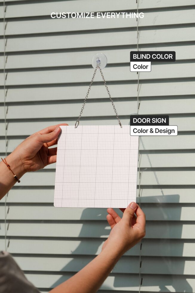 Hand holding blank pink grid paper door sign hanging on chain against striped background