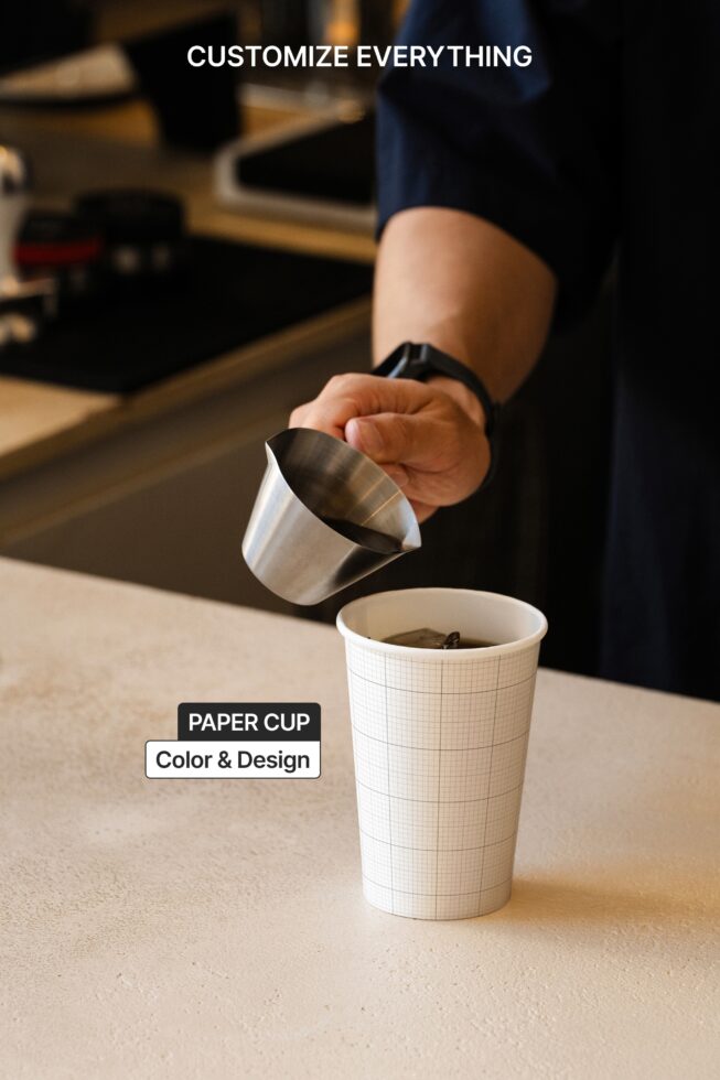 Barista pouring steamed milk into gridded paper coffee cup on wooden counter