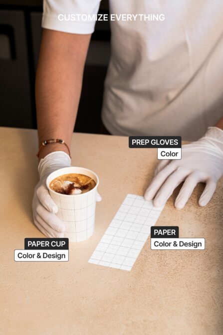Hands wearing white gloves holding paper cup, stationery on beige table