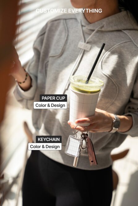 Person holding customizable paper cup with straw in sunlight, keychain attached