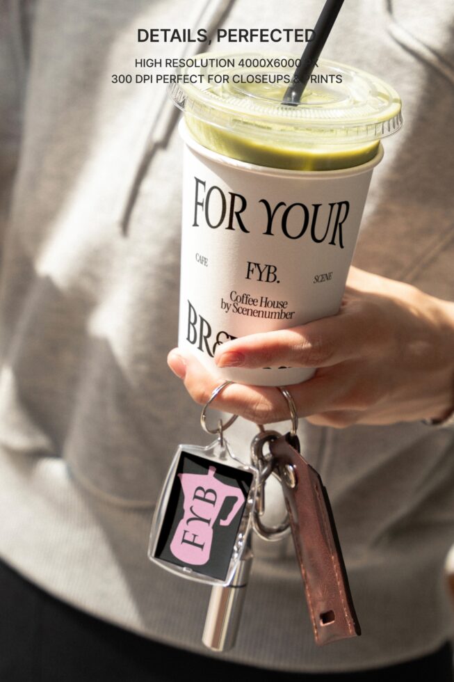 Hand holding branded coffee cup with matching keychain on brown leather strap outdoors