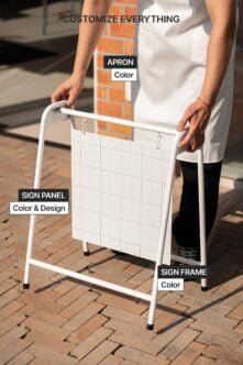Hands positioning white A-frame stand with blank sign panel on brick paved outdoor area