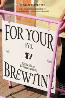Hands holding vibrant pink sandwich board sign with white panel featuring coffee shop branding