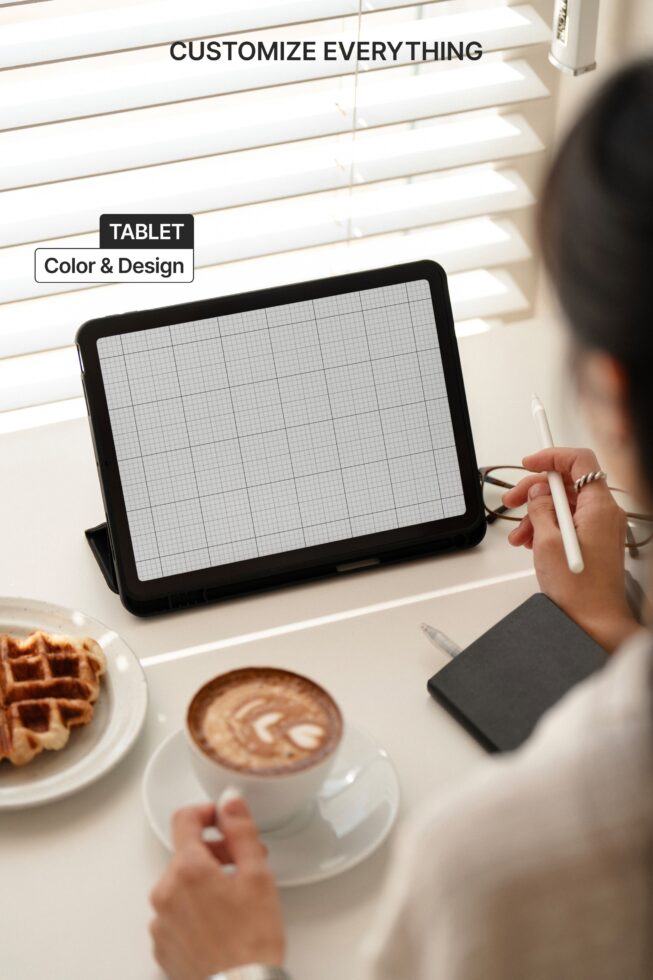 Black tablet device mockup held at angle with coffee, pastry, studio workspace setup