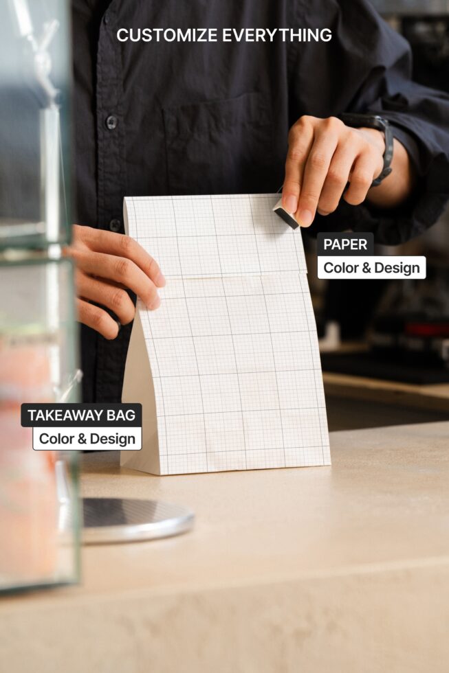 Hand holding takeaway paper bag mockup with grid background, indoor cafe setting