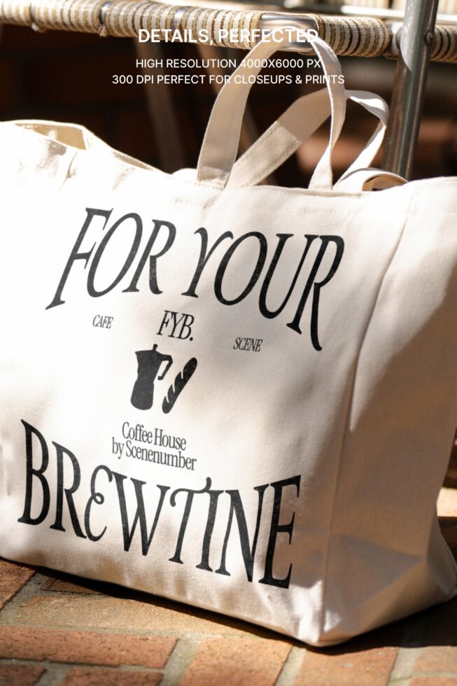 Cream canvas tote with black text sits on woven chair outdoors by brick wall