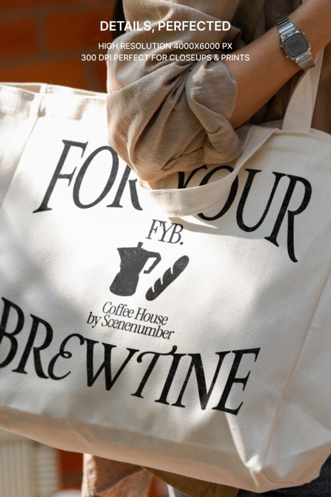 Overhead shot of cream tote with typography detail folded on person wearing watch in warm lighting