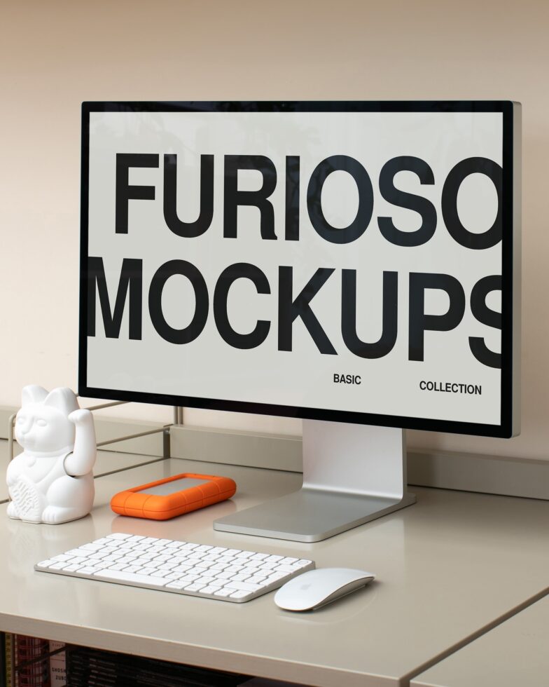 Desktop setup with monitor, keyboard, mouse, white figurine, orange device