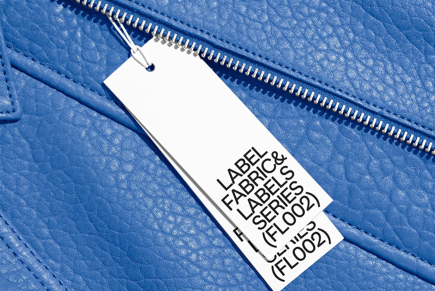 White fabric label on bright blue textured leather with metal zip detail