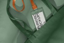 Clear square fragrance bottle with orange label on sage green fabric