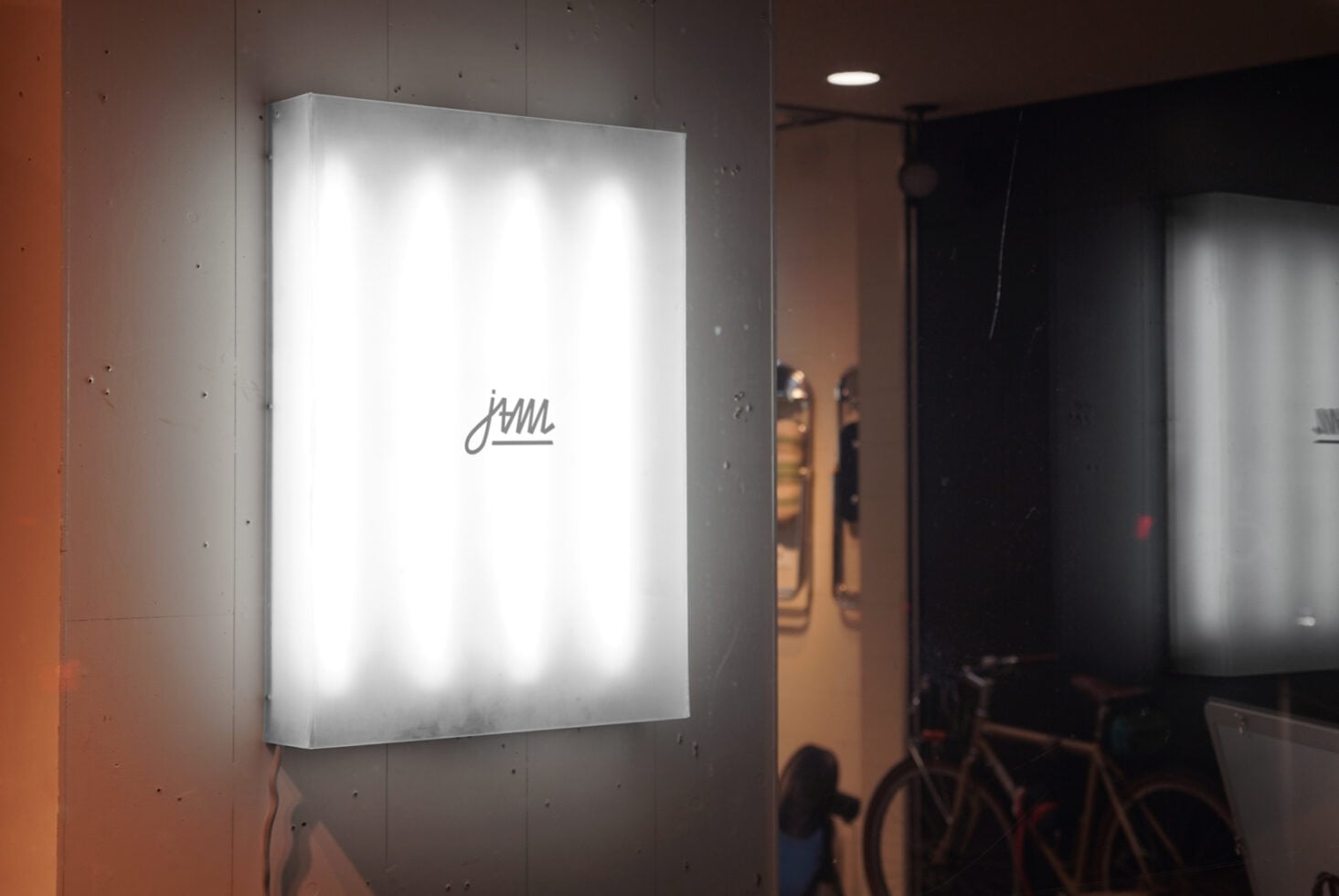 Minimalist white illuminated lightbox with cursive script logo on concrete wall