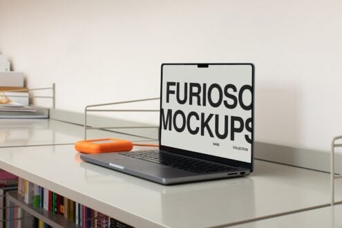 MacBook on white desk showing white screen with bold black type, orange mouse beside it