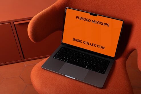 Laptop with orange screen on burnt orange fabric chair in moody lighting