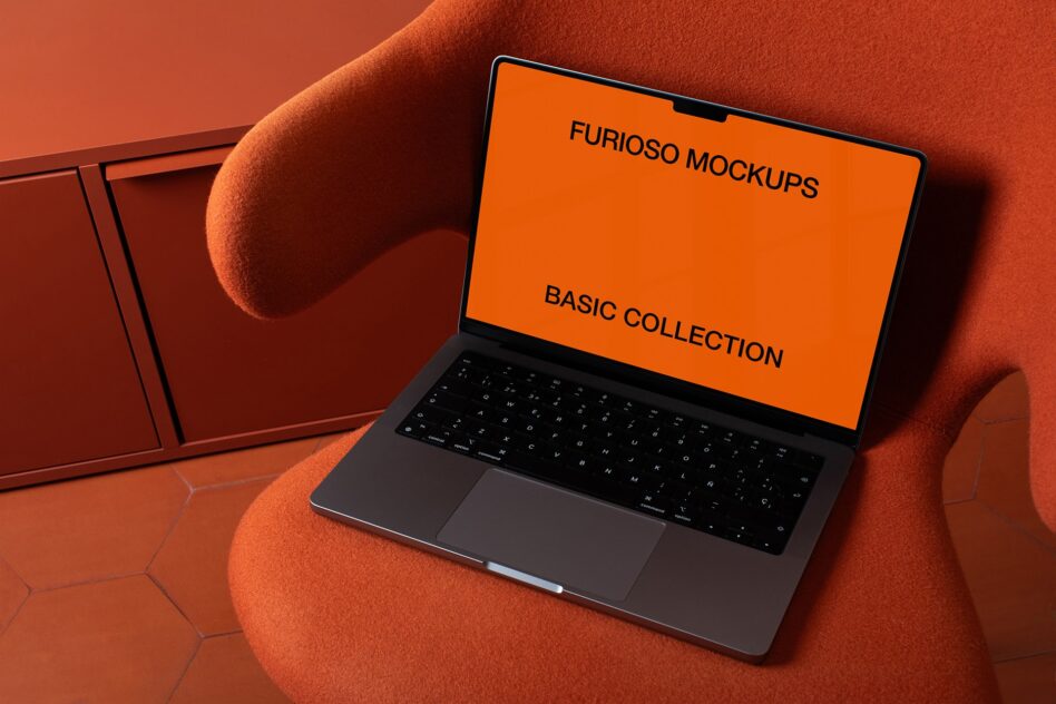 Laptop with orange screen on burnt orange fabric chair in moody lighting