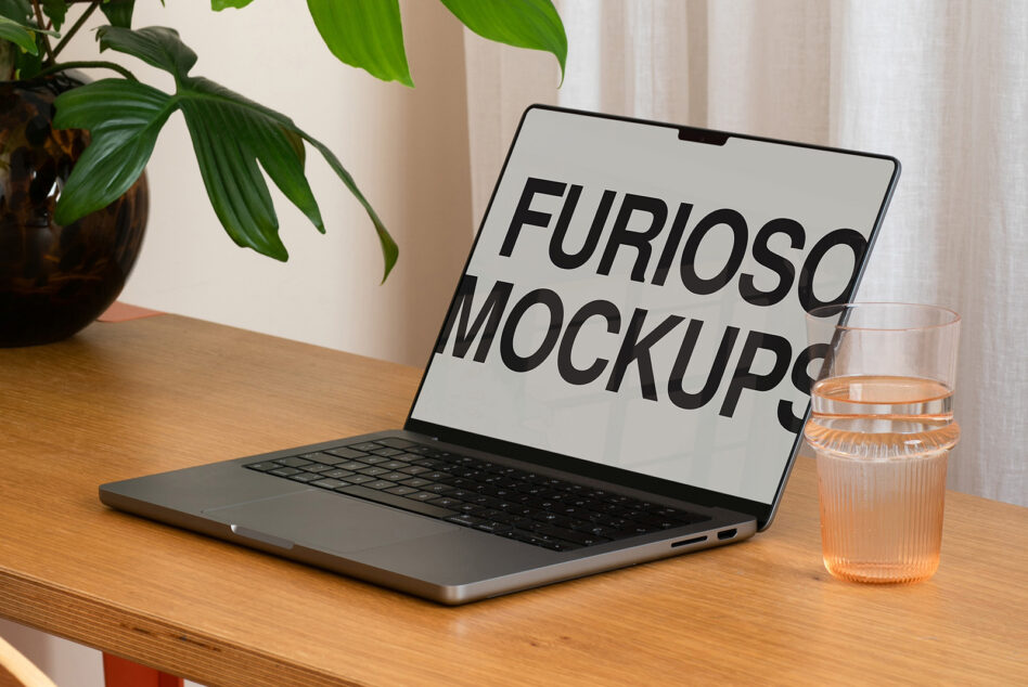 Laptop with white screen displaying Furioso Mockups text on desk with water glass