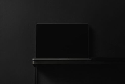 Closed laptop with dark screen angled against black studio backdrop