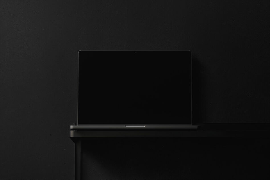 Closed laptop with dark screen angled against black studio backdrop