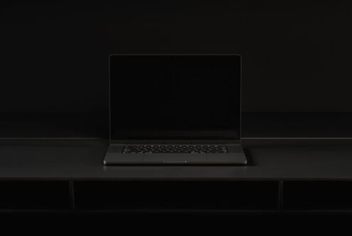 Dark laptop sitting on black desk with blank screen mockup in studio lighting
