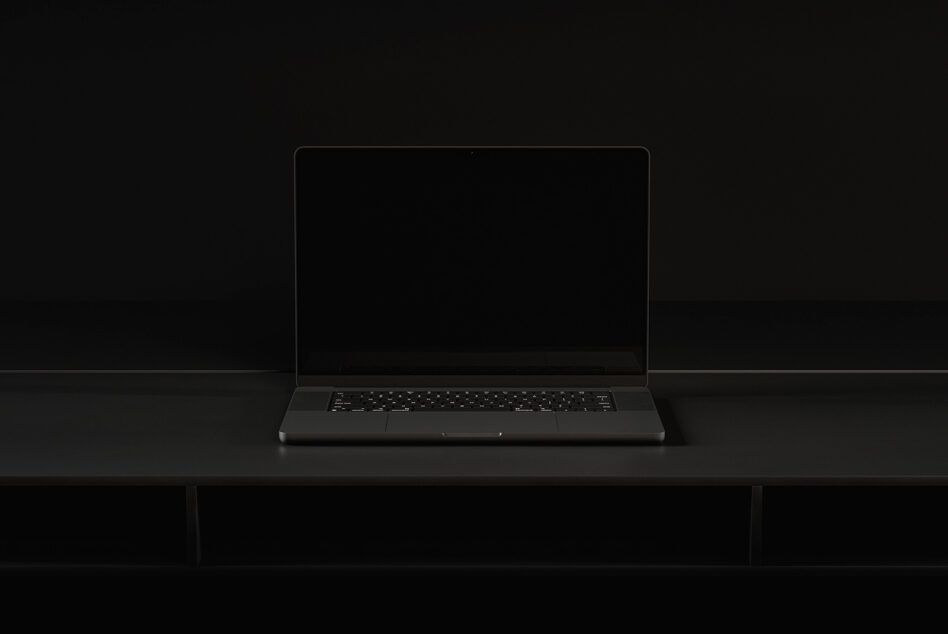 Dark laptop sitting on black desk with blank screen mockup in studio lighting