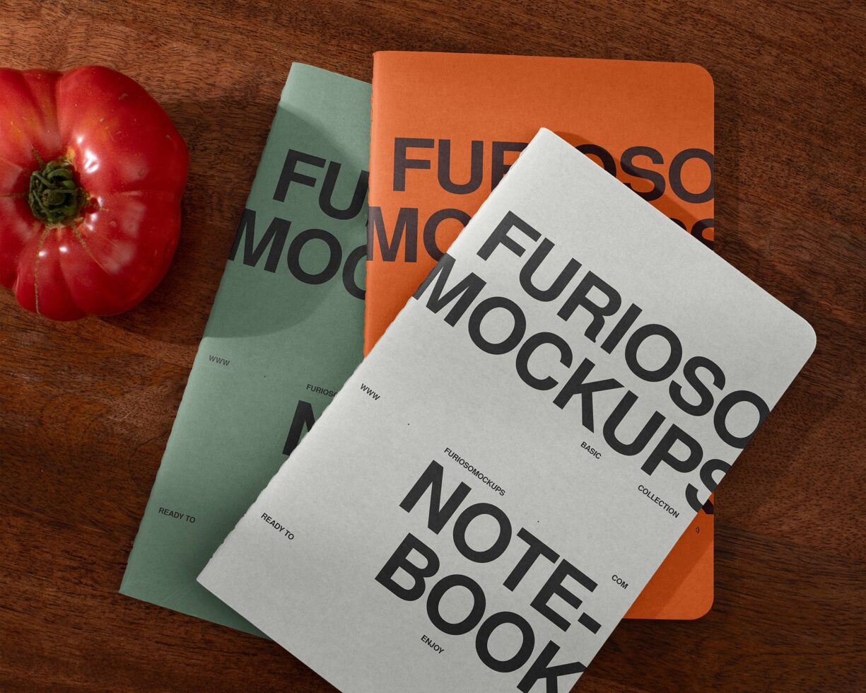 Three notebooks fanned out with fresh tomato, mixed colors on rustic wood surface