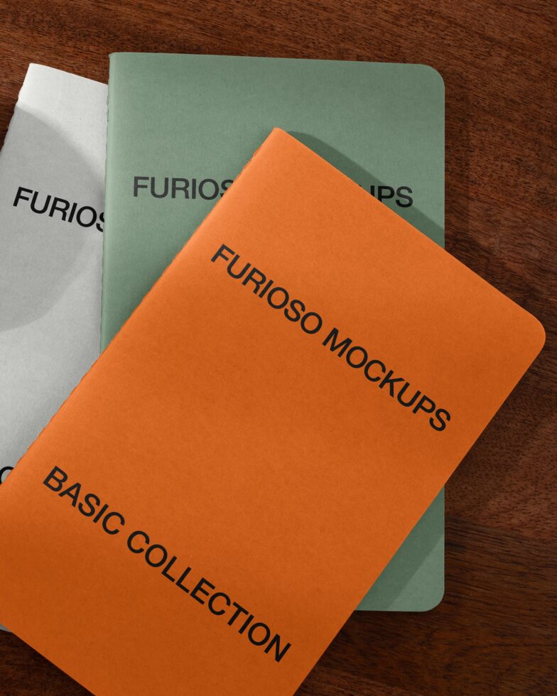 Stacked notebooks in orange, white, green on wooden table with soft shadows