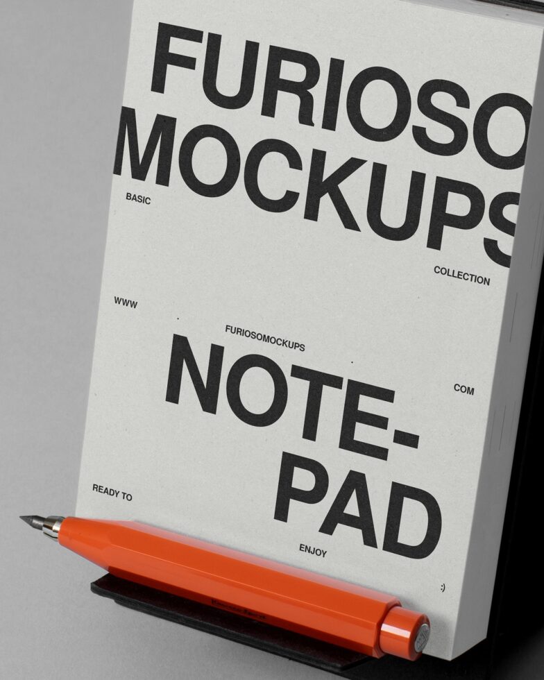 Notepad mockup with bold black text on cream cover, orange pen resting at bottom, angled view