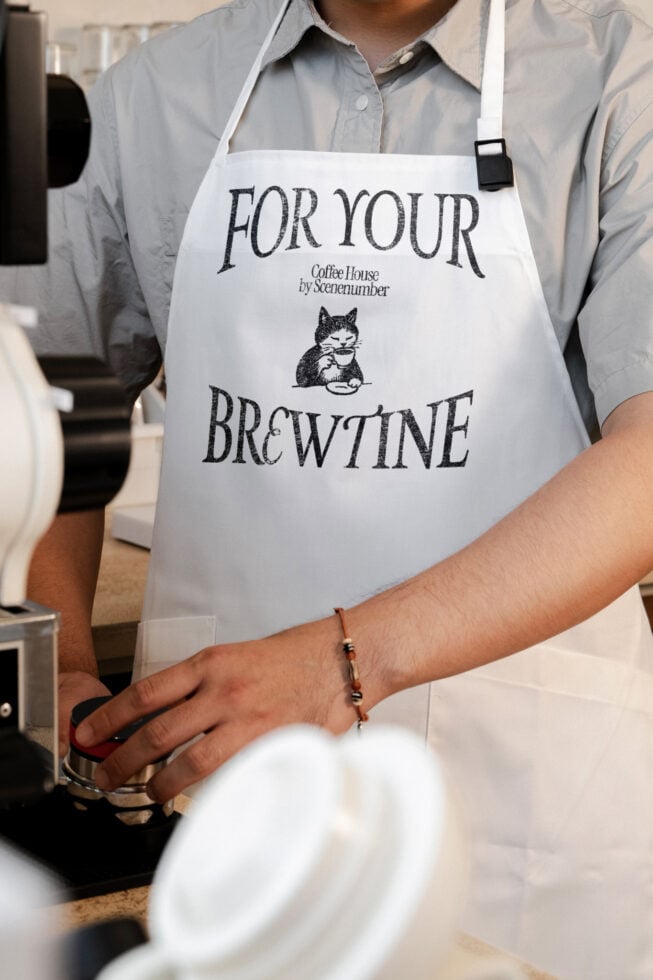 White apron with For Your Brewtine coffee house text with cat holding cup graphic