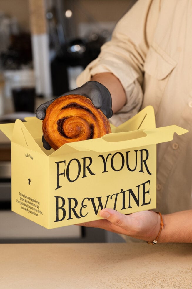 Yellow takeout box with spiral pastry inside held in hands with black gloves