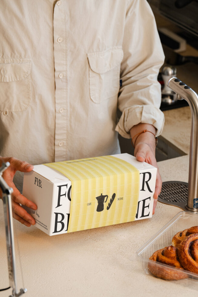 Hands presenting yellow striped bakery box with custom branding, croissants nearby