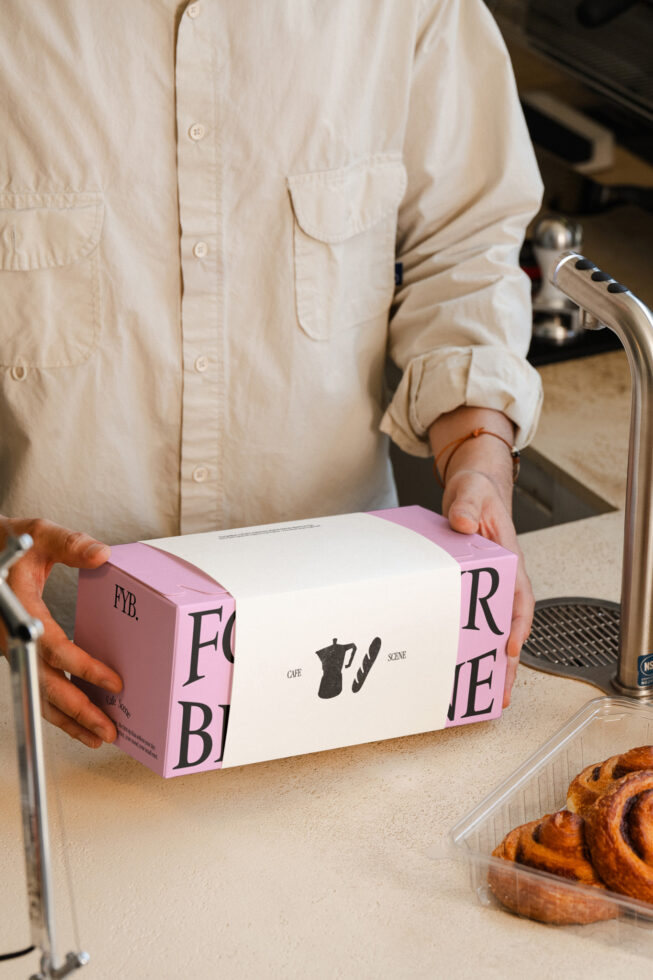 Hands holding pink bakery box with pastry, coffee shop branding visible, mockup