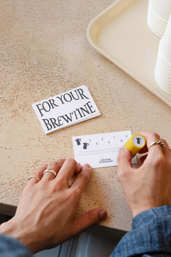 Hands stamping a coffee shop punch card on a cork surface with cups
