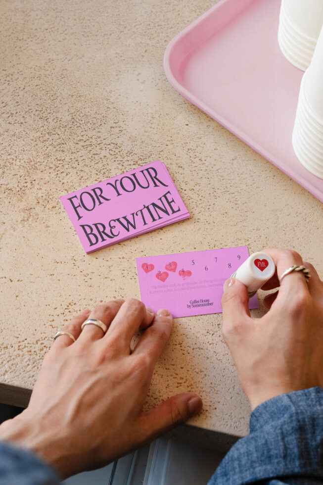 Overhead shot of pink loyalty card with hearts, stamp, next to pink tray, coffee cup