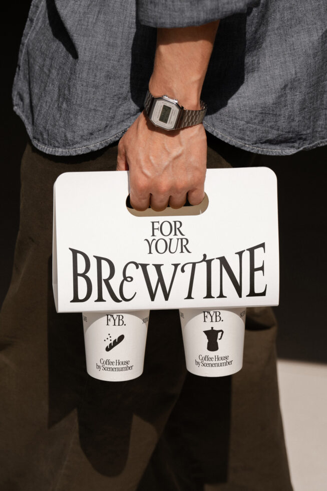 Man holding white paper bag with coffee cups below, metal watch on wrist