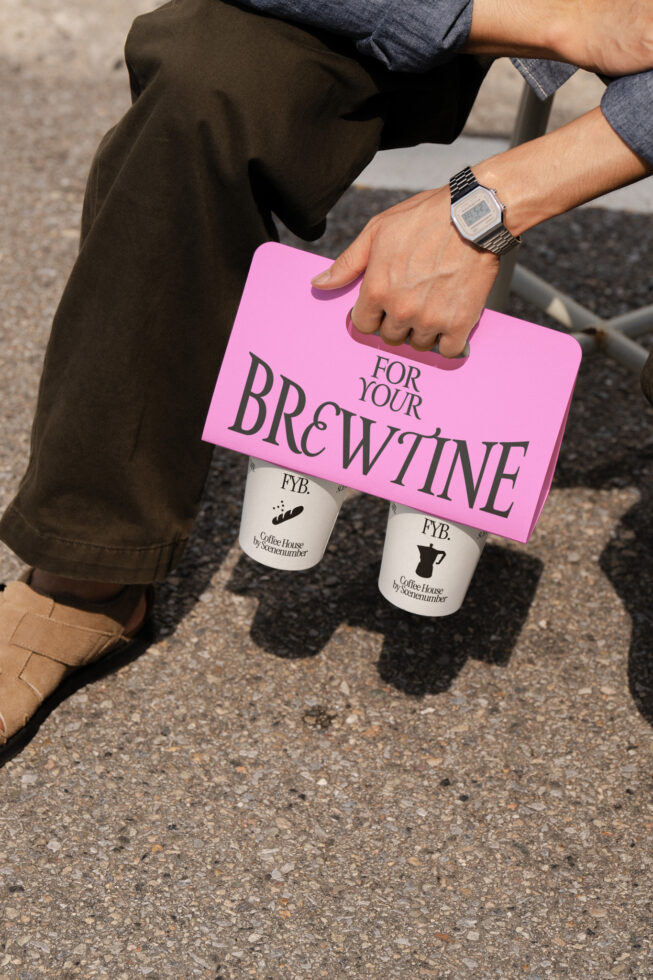 Person carrying hot pink paper bag with two white coffee cups below on street
