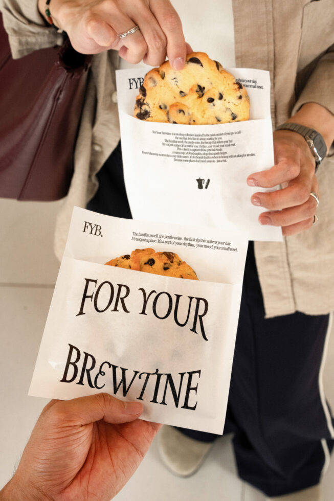 Two hands holding cream paper bags with chocolate chip cookies peeking out