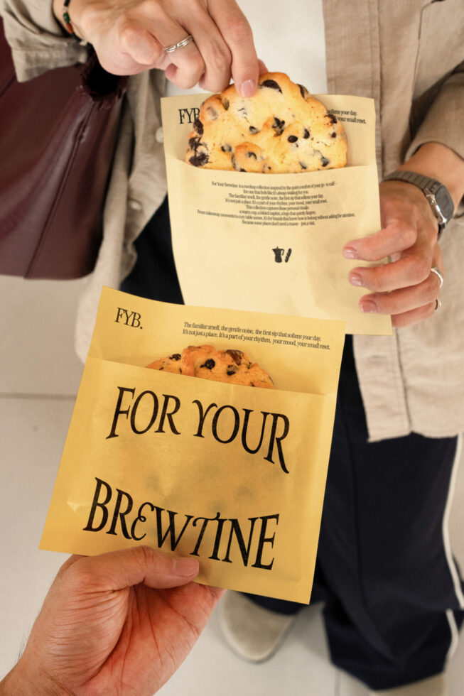 Two hands holding cream paper bags with chocolate chip cookies peeking out