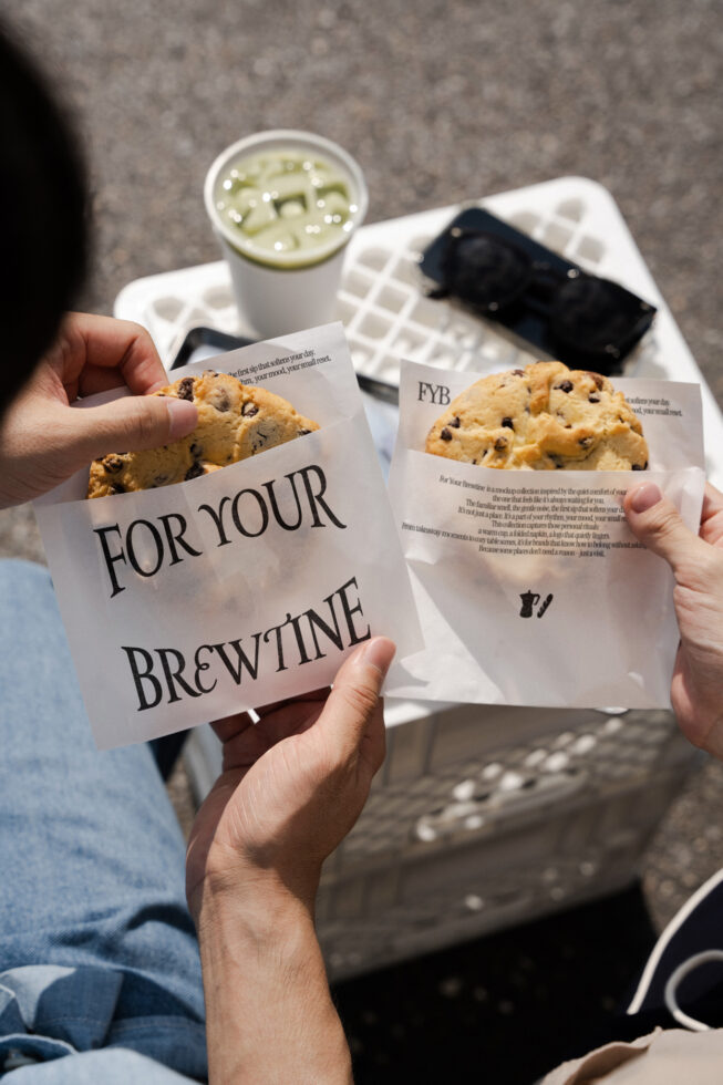 Beige paper bags stuffed with chocolate chip cookies held in hands