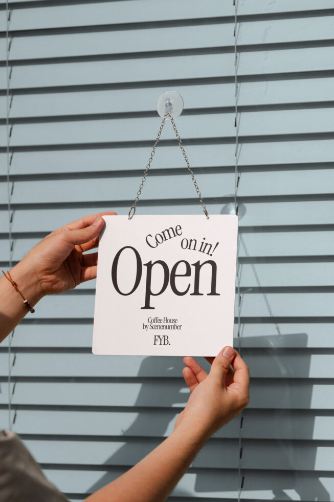 Cream sign hanging from suction cup reads Come on in Open for coffee shop