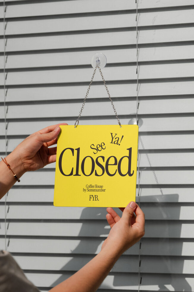 Bright yellow closed sign hanging on white louvered doors with chain